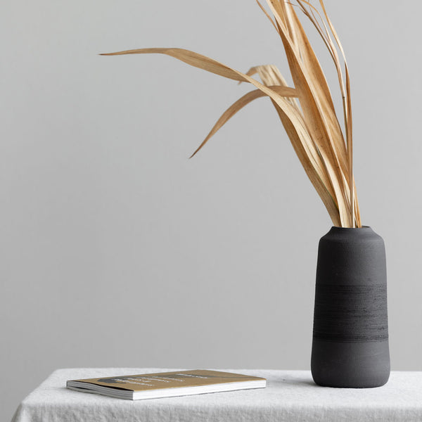 Handmade ceramic vase in black with a ribbed texture used for dried stems and floral arrangements