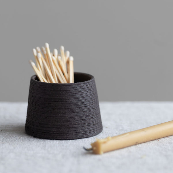 Handmade ceramic match striker in black clay body with a ribbed texture to hold and light matches
